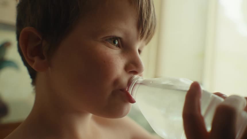 Close up of a young boy drinking from a water bottle in his house