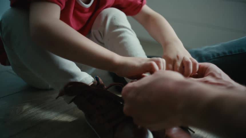 Young boy on the floor getting help to tie his shoes, the boy raises his arms and smiles in excitement