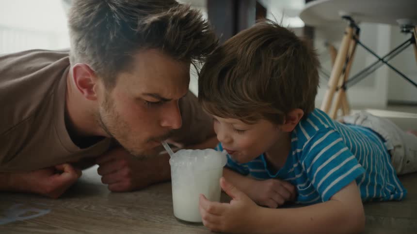 Father making bubbles in milk as his young son plays along at home
