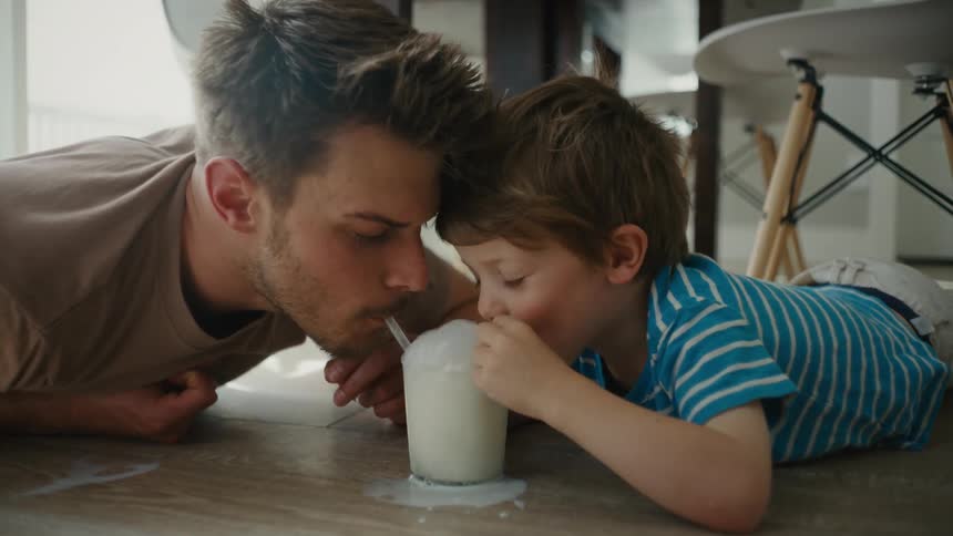 Father and young son sharing pure joy as bubbles overflow from a glass of milk at home