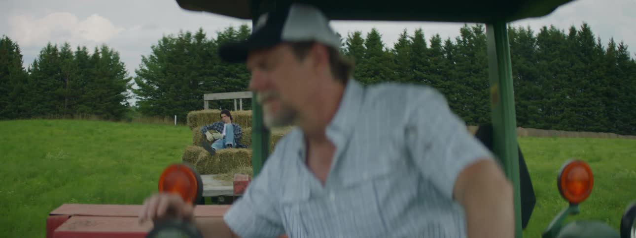 Farmer drives tractor pulling trailer with person and haybales