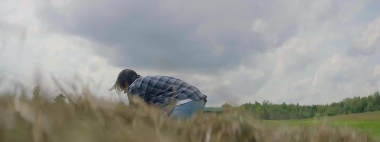 Worker man piling haystacks outside in a farm with another worker on a truck parked at a distance