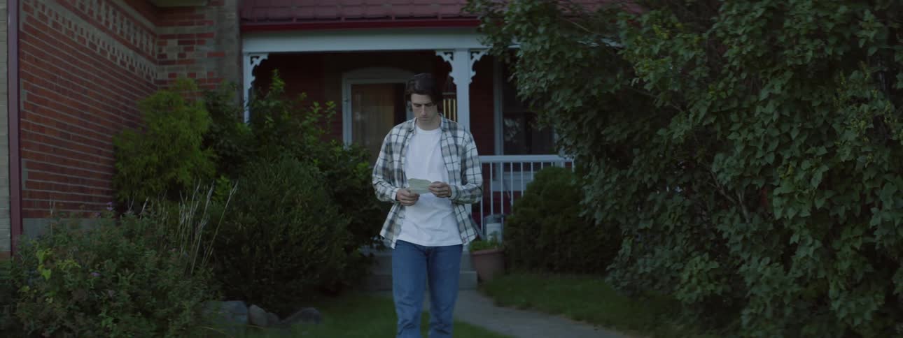 A man reads a note while walking away from a house during the day