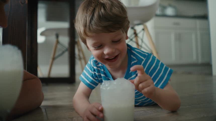 Young boy laughing as milk bubbles tickle his nose at home