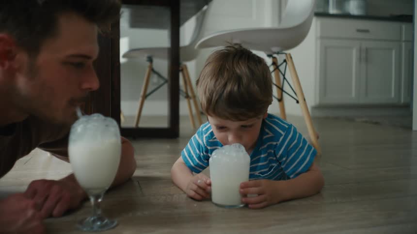 Little Boy Laughs With His Father While Blowing Bubbles in Milk at Home