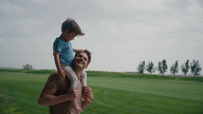 Father standing with young son on shoulders in a quiet moment of connection outdoors