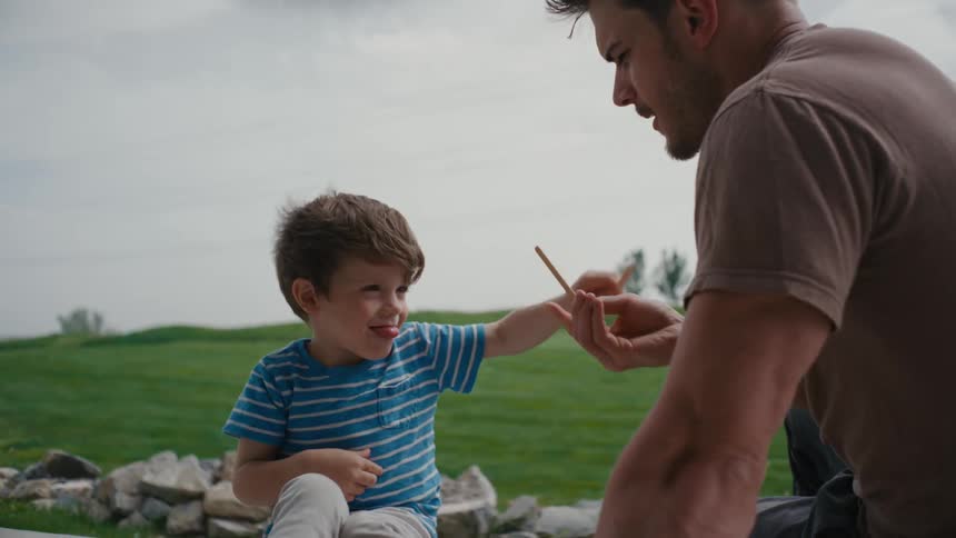 Father and son sharing a playful, lighthearted moment sword fighting with popsicle sticks outdoors