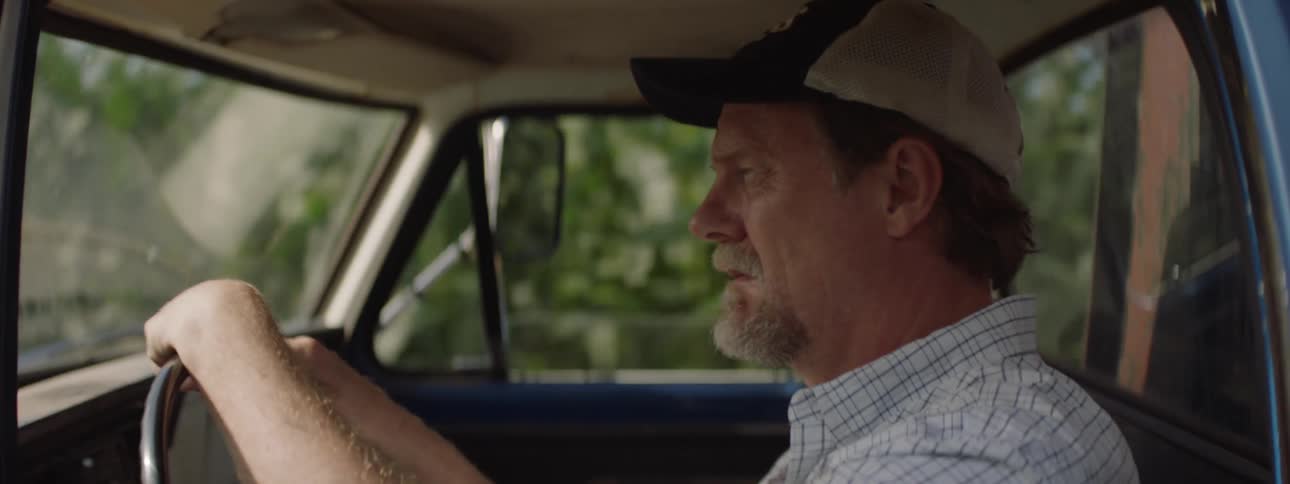 Bearded man wearing a baseball cap driving a car looking nervous and lost