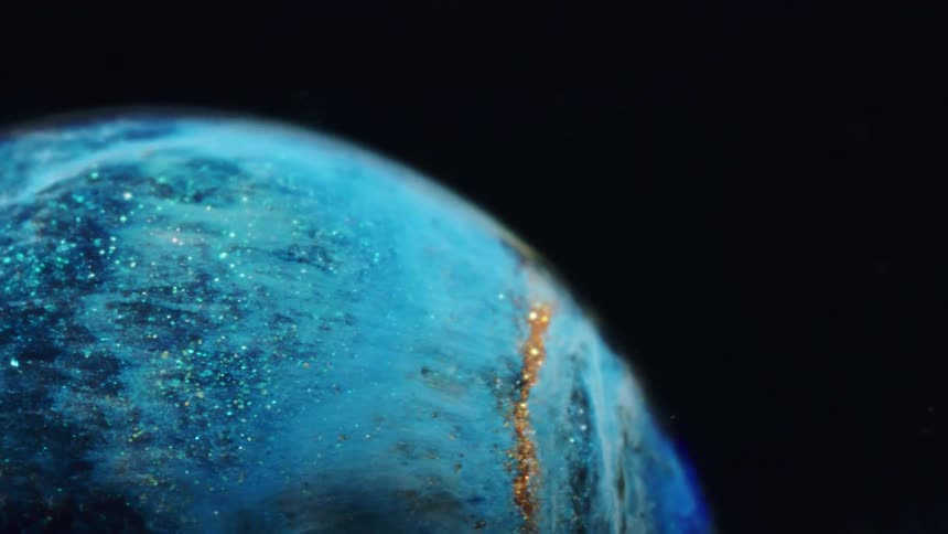 A glowing blue planet with twinkling lights rotates as it moves across the darkness