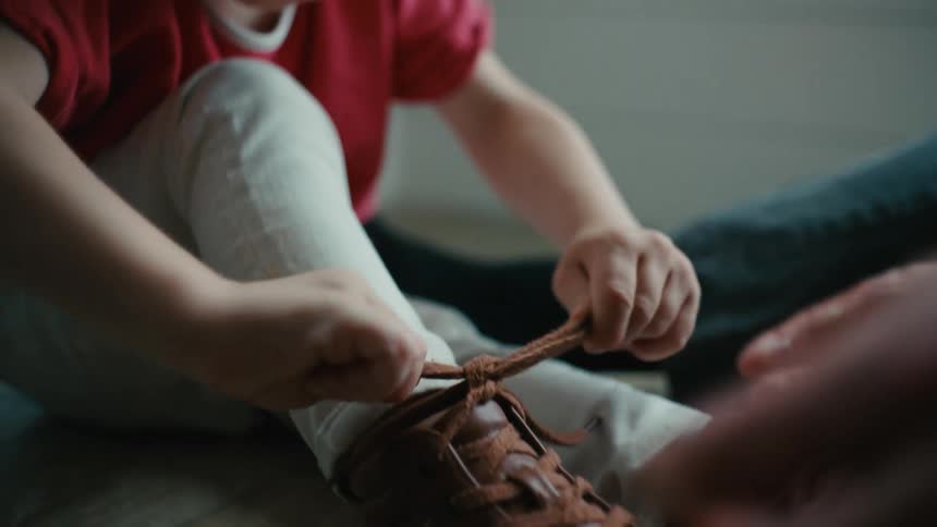 An adult teaches a young boy how to tie his shoelaces