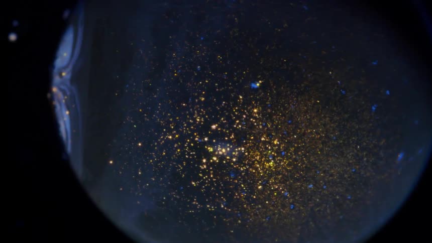 A globe with gold glittering lights inside rotates as it moves across the darkness among small orbs in the distance