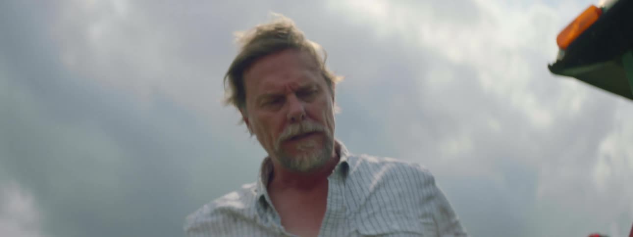 Bearded man next to a parked tractor checking a malfunctioning machine and getting upset over it