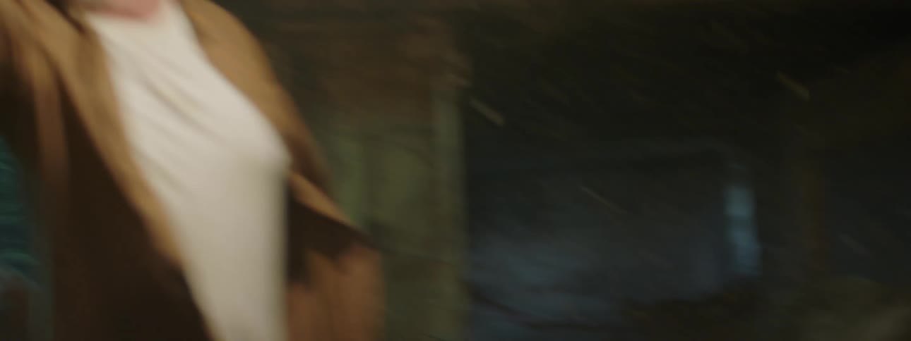 Farmer in a barn herding cows in while the weather blows in debris behind him and he yells at someone near him