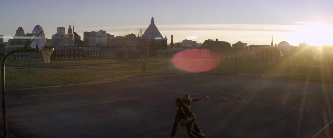 Two men play basketball on a court at dawn