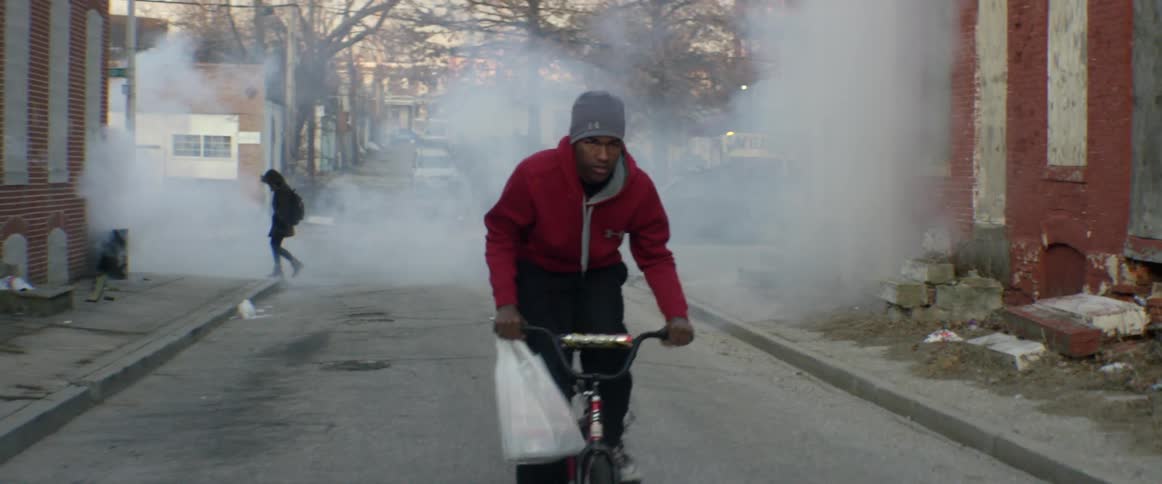 A man is riding his bike down a street with a bag