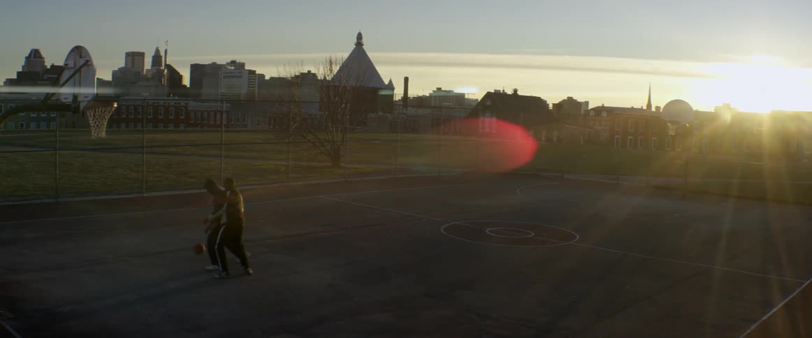 Two people are playing basketball on a court at sunset