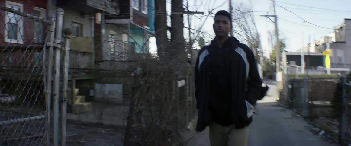 A man is walking down an alley as another runs behind him