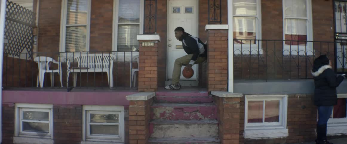A boy leans against a brick wall and dribbles a basketball