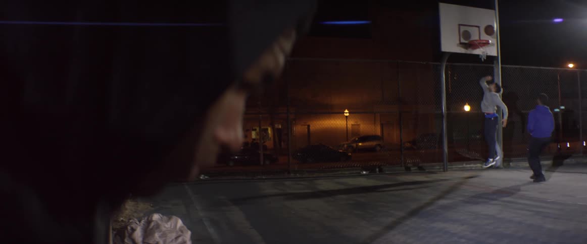 A young man looks at the ground while a basketball game goes on in front of him