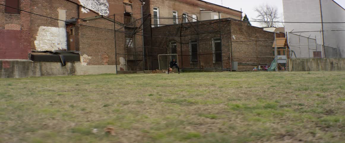 A boy stands in a grassy lot and dribbles a basketball