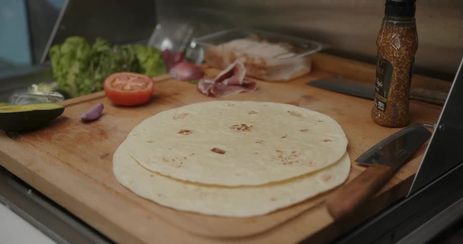 Cook places tortillas on chopping board between knives and produce