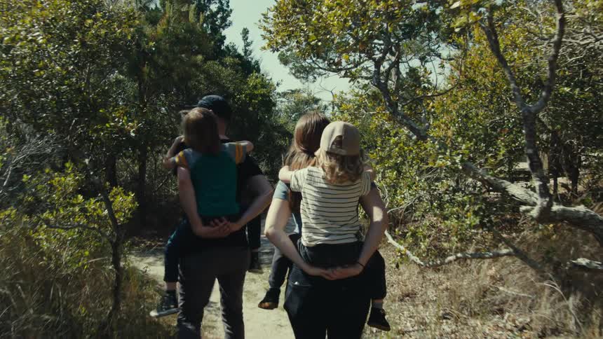 A nature trail outdoors with a man and woman both carrying children on their backs