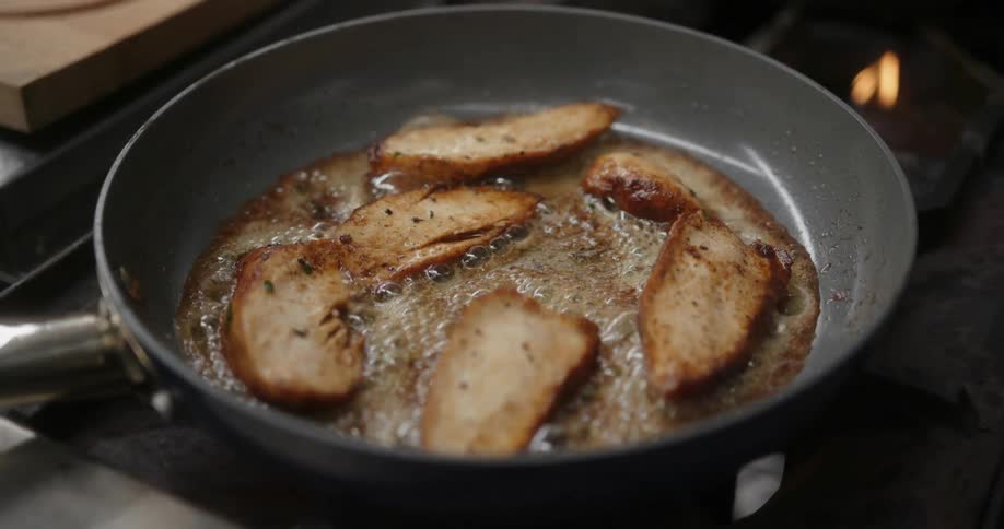 A close up of five meat slices sizzling in a pan on the stove