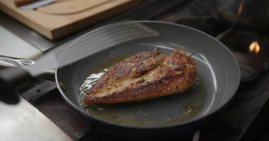 Close up of chicken being fried on a pan and flipped with a spatula by a person wearing gloves