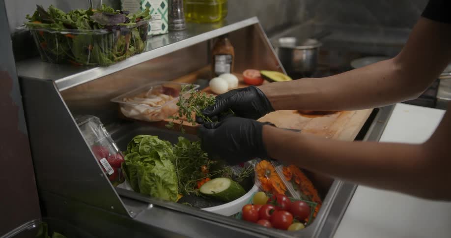 A person wearing gloves in the kitchen cooking and picking up vegetables from a bucket