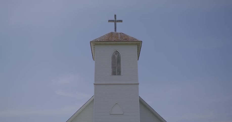 A cross atop the steeple of a church under a clear daytime sky