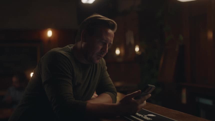A man sitting at a restaurant bar leaned over pulling out his cell phone before getting served three beers in glasses