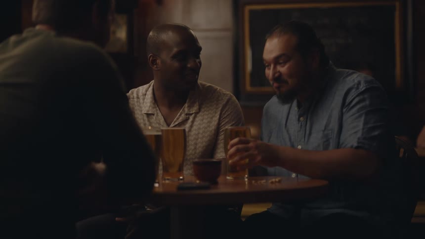 Three friends sitting at a table in a bar chatting and enjoying their beers