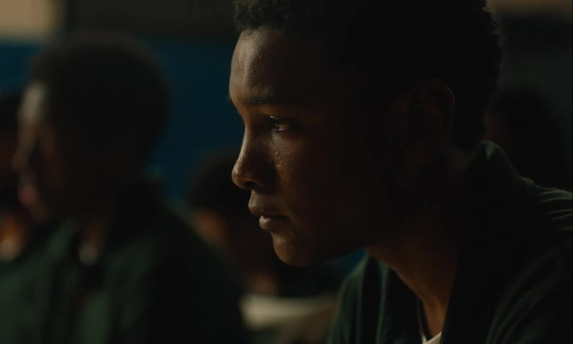 Teenage boy sitting near other boys as he looks down sadly in contemplation