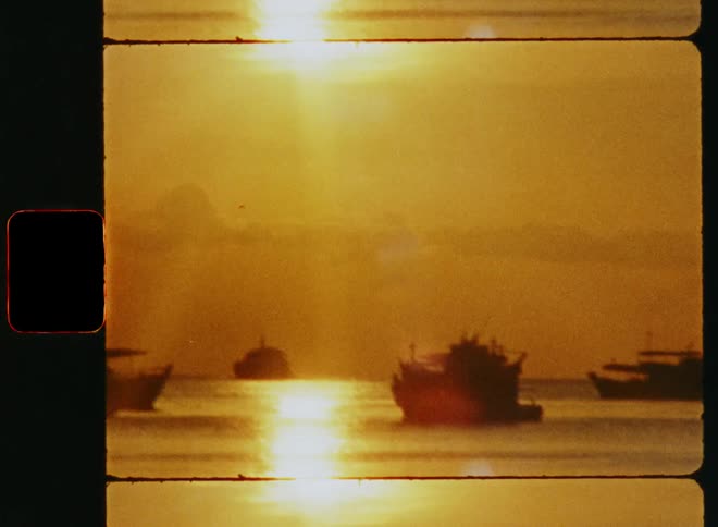 A group of small boats sit in the water near the shore during a sunset