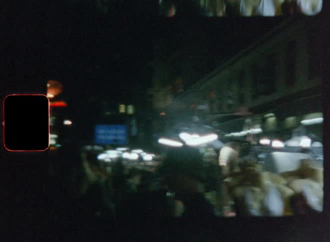 Pedestrians walk along street at night passing merchandise set near the street