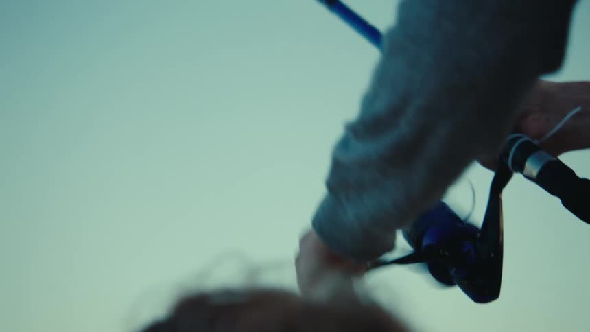 A close up of a man reeling a fishing pole while standing next to a small child