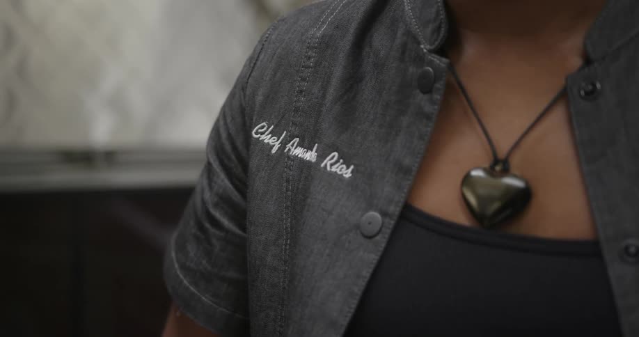 A woman wearing a shirt that identifies her as a chef wears a necklace with a black heart hanging from it