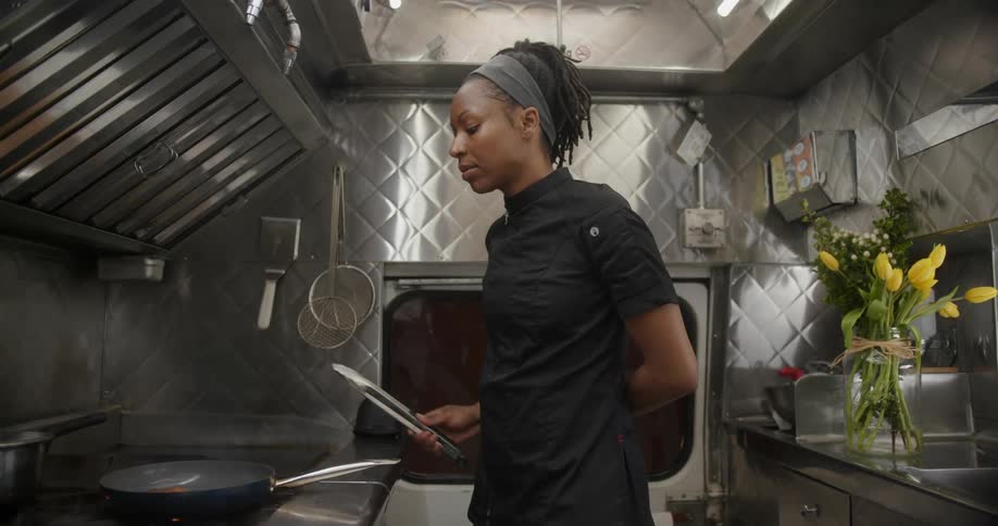 Young woman chef standing in a food truck using tongs to prepare food on a stove