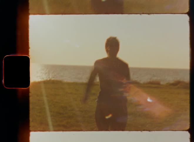 Young jogging woman sprints through a field towards the ocean trying to run away in the evening light of a warm autumn day on old Super-8 film footage with lens flare