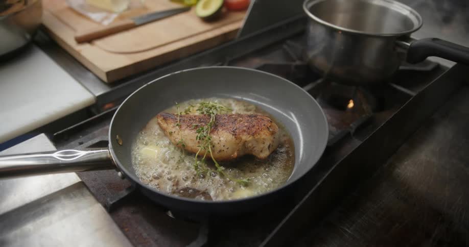 A person adds fresh herbs to pan fried chicken