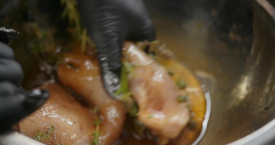 A close up of a person wearing black gloves while mixing chicken in a bowl with other ingredients