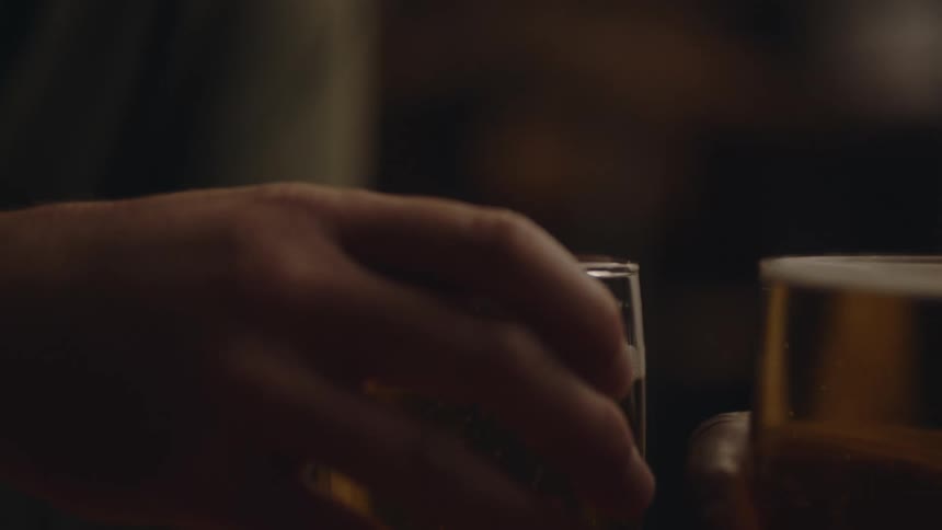 Close up of two glasses with alcoholic beverages in them as two people pick up the glasses and drink from them