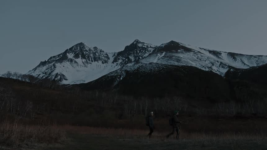 Two people are hiking near a mountain range