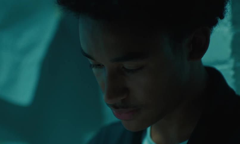 A close up of a young male sitting looking down and talking before looking up in front of him
