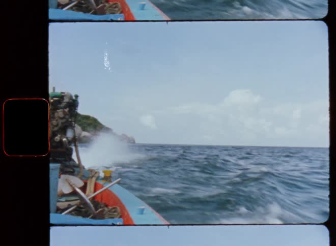 A small boat packed with equipment sailing over ocean waves leaving mountains behind it