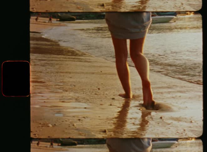 Woman walking along a sandy shoreline leaving foot prints in the sand as a wave splashes against her feet