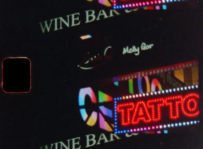 Neon store signs on a city strip at night lit up and flashing