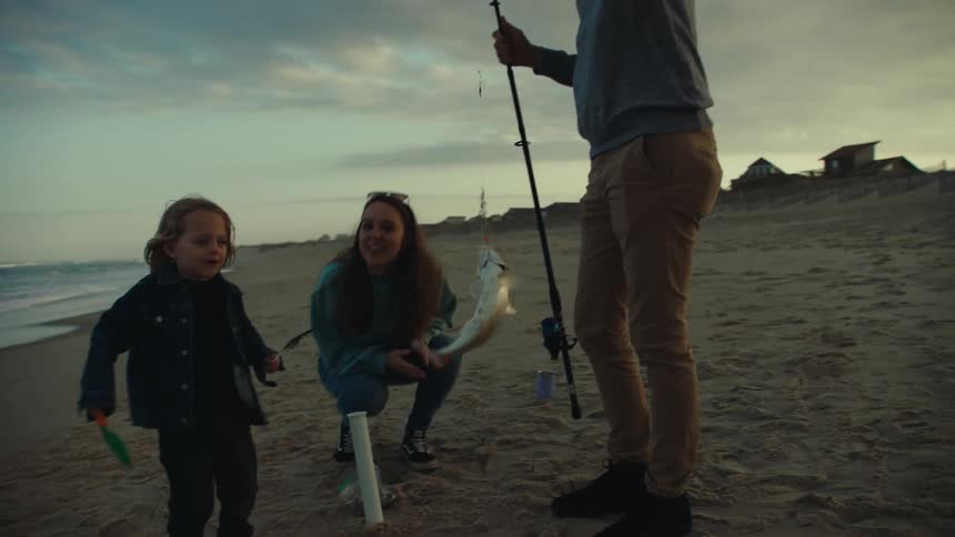 Father proudly displaying the fish he caught on his fishing rod to his family and young son at the beach
