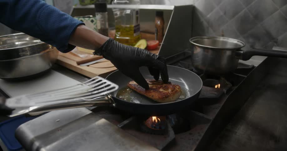 Someone cooking meat in a frying pan on the kitchen
