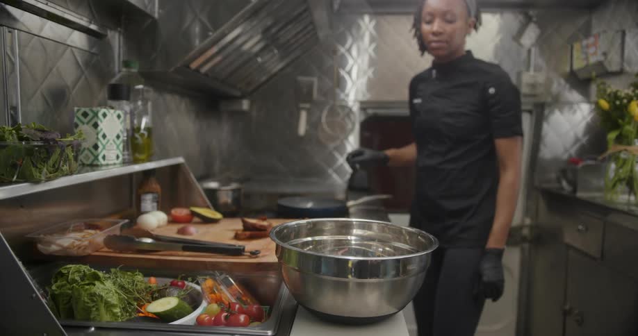 A black woman in the kitchen preparing a meal while dragging a stainless steel bowl